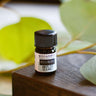 Megan & Co Boji Bliss essential oil mini bottle on wooden block with eucalyptus leaves.