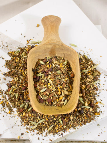 Megan & Co. Winter Warmer loose leaf herbal tea blend with raw ginger root, cinnamon chips, and holy basil on a wooden scoop on top of a white plate for seasonal immune support.