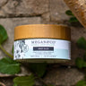 Megan & Co. Mint Aloe body cream jar with a bamboo lid on a rough stone surface, staged with fresh green mint leaves and rustic branches with a rope overhead.