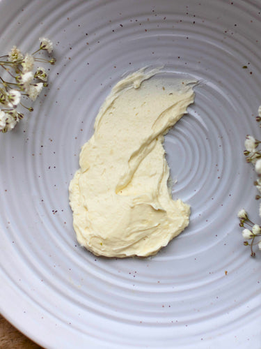 A thick swatch of pale yellow herbal nursing cream on a white textured plate with baby's breath flowers.