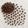 A small pile of dark brown, crushed cacao nibs scattered across a white marble surface.