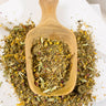 MEGAN & CO. Loose-leaf herbal tea, Peaceful Prairie blend, dispensed into wooden scoop on a marble white counter.