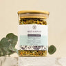 A glass jar containing dried herbal tea leaves with a label that reads 'Peaceful Prairie Tea Blend'. The jar is placed on a neutral background alongside some green foliage.