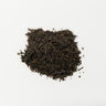 A small mound of dark loose leaf black tea, characteristic of an Earl Grey blend, centered on a clean white surface.