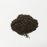 A small, centered mound of dark, fine-cut loose leaf black tea characteristic of an English Breakfast blend on a plain white surface.