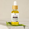 A glass dropper bottle of Revival Hair Oil by MEGAN & CO. Apothecary, placed on a white surface with a green leaf in the background.