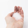 A person's open palm holding a generous pile of translucent, medium grain Epsom salt crystals against a bright white background.