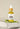A small clear glass bottle with a dropper filled with yellow liquid, labeled 'Megan and Co R + R Herbal Oil', displayed on a white textured surface with a green leaf beside it.