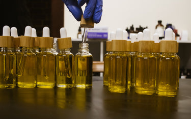 Person filling dropper bottles with a yellow liquid in a laboratory setting.