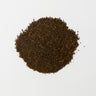 A rounded mound of dark, rich brown roasted chicory root granules centered on a stark white background.