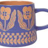 A periwinkle blue ceramic mug featuring a wax-resist artisan design of tan floral patterns and geometric borders near the base. The interior of the mug is a contrasting earthy tan color.