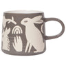 A profile view of a charcoal-grey ceramic mug featuring a wax-resist artisan design of a white rabbit, a crescent moon, a rainbow, and floral elements. The mug has a rounded handle and a clean white interior.
