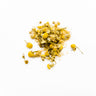 A small, delicate mound of dried chamomile flowers with prominent yellow centers and white petals, some with green stems attached, scattered on a clean white surface.