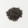 A small, rounded mound of tiny, dark purple-to-black dried elderberries centered on a clean white surface.